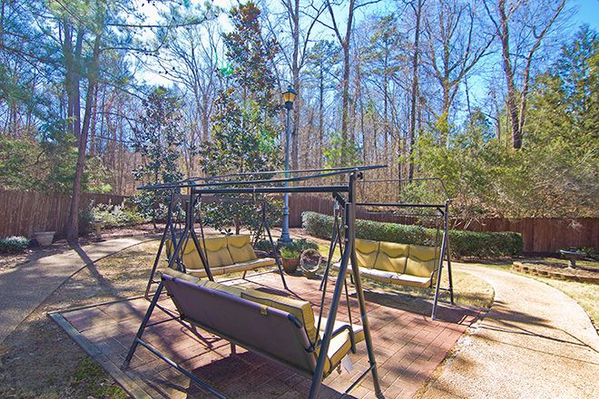 A sunny backyard features swings and garden furniture surrounded by trees.