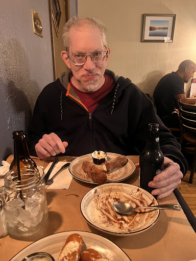 A man enjoying a meal at a cozy restaurant, featuring dessert on the table.