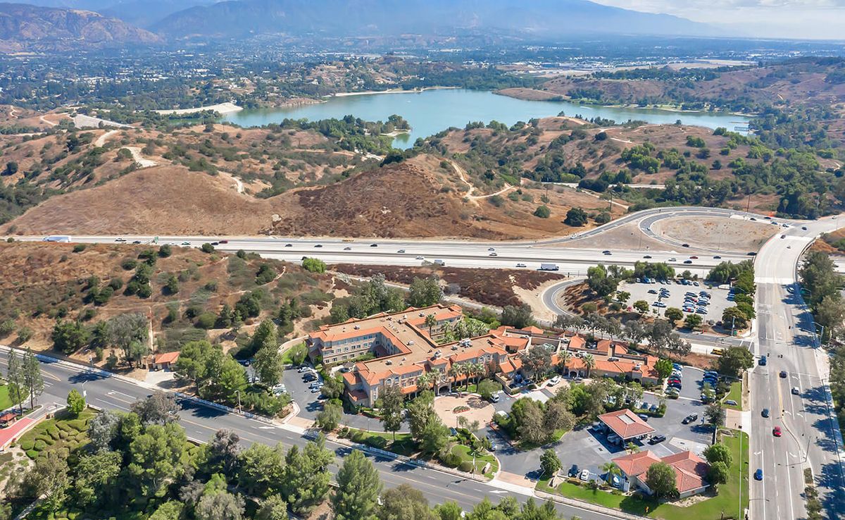 A scenic aerial view showcasing a lake, highway, and surrounding hilly landscape with buildings.