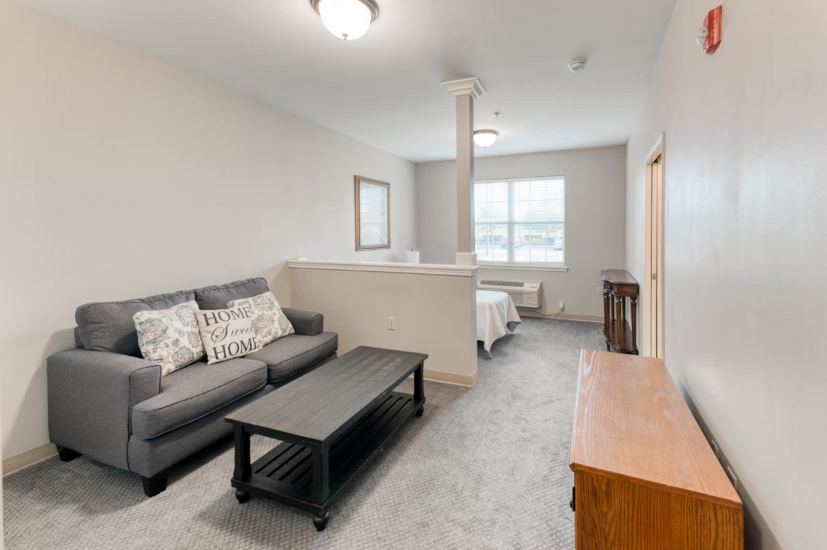 A cozy living room with a grey sofa, coffee table, and a window providing natural light.