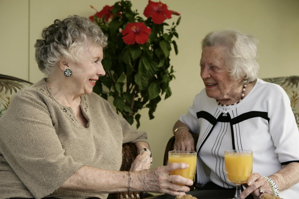 Two elderly women enjoying a conversation over glasses of orange juice.