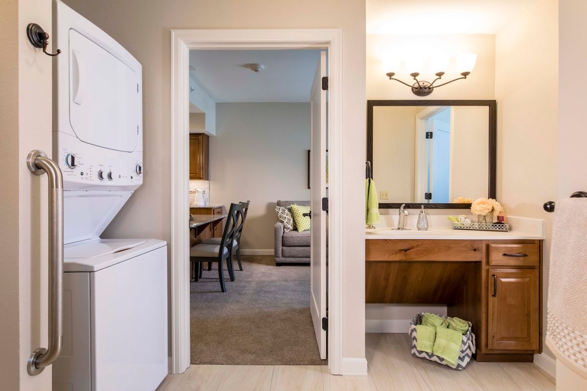 A cozy apartment interior featuring a stackable washer and dryer, view into a living room, and bathroom with a well-lit vanity.