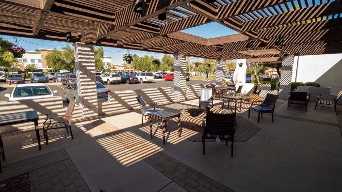 An outdoor seating area with a pergola casting striped shadows on a sunny day.