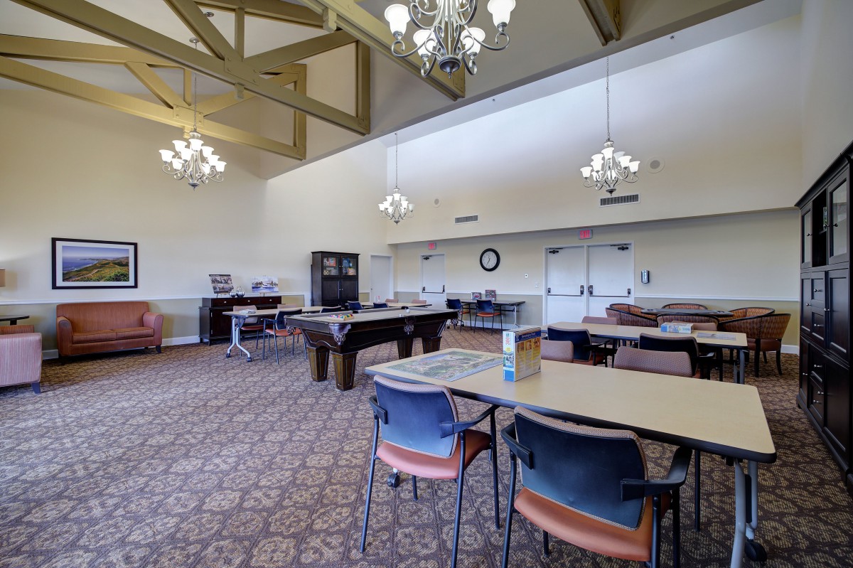 A spacious recreation room with a billiards table, chairs, and tables under elegant chandeliers.