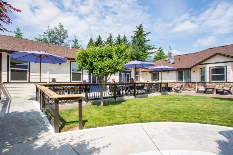 A cozy backyard with a well-maintained lawn, wooden deck, and outdoor seating under umbrellas on a sunny day.