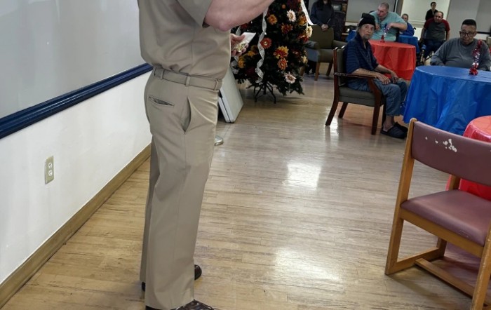 A person in a uniform stands indoors, possibly giving a presentation.