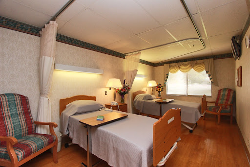 A shared hospital room equipped with two beds, bedside tables, and natural light streaming through the window.