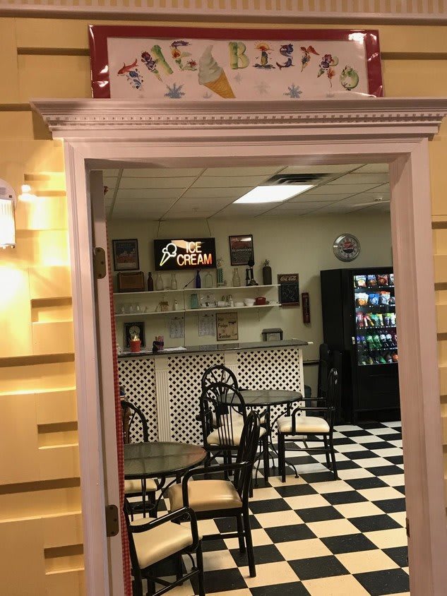 A retro-style diner with a black and white checkered floor, tables, chairs, and a vending machine in the corner.