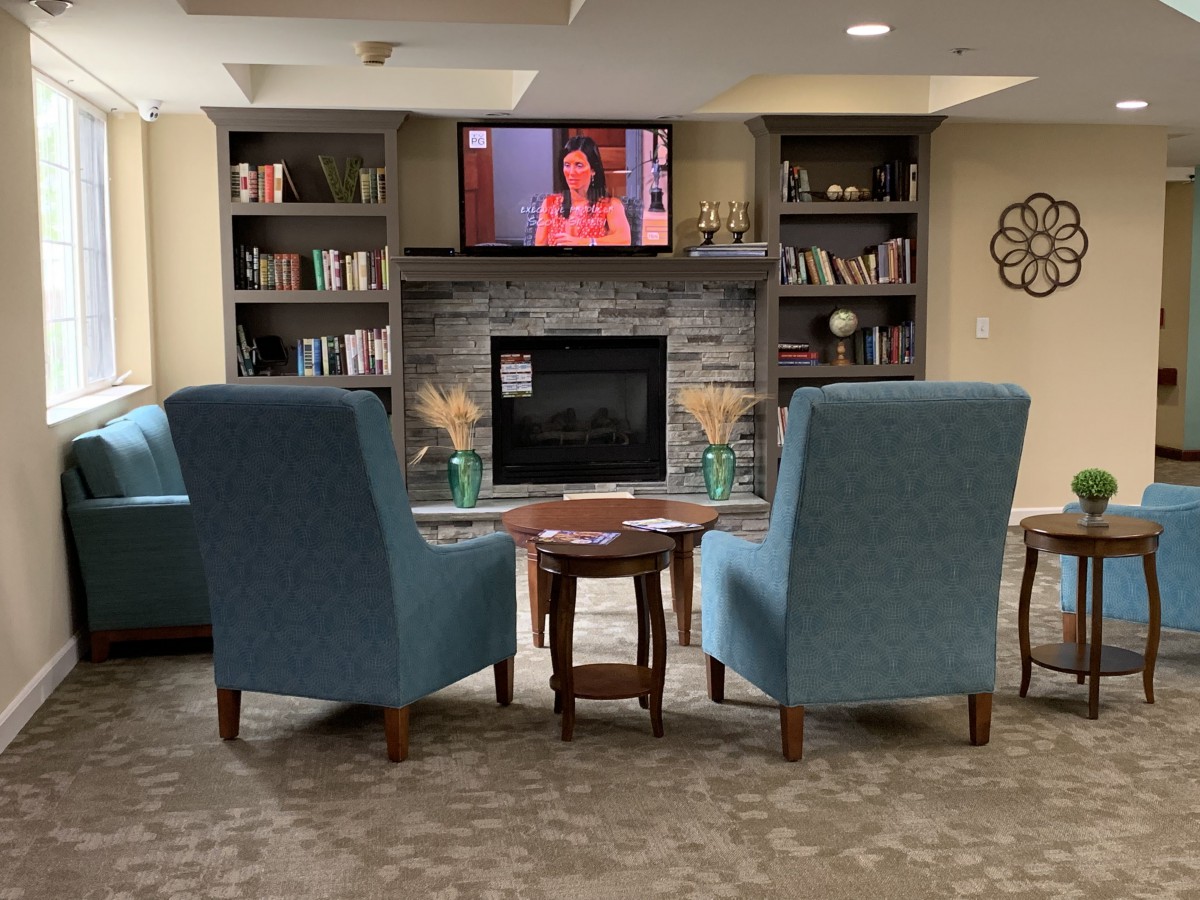 A cozy living room with two armchairs facing a fireplace, bookshelves, and a television mounted above.