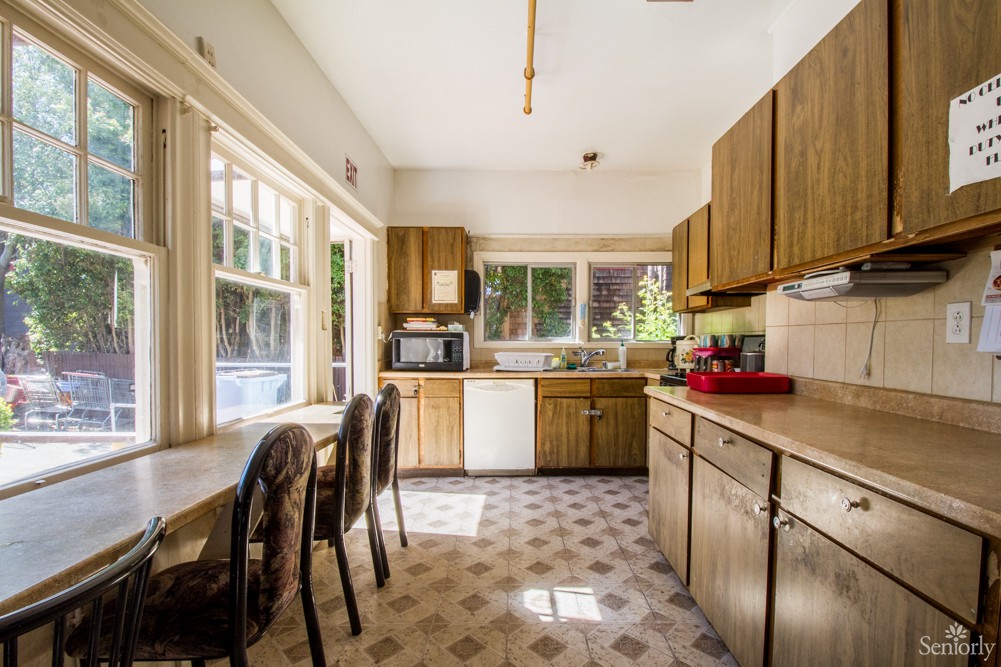 A modern kitchen with wood cabinets, a dining table, and large windows.