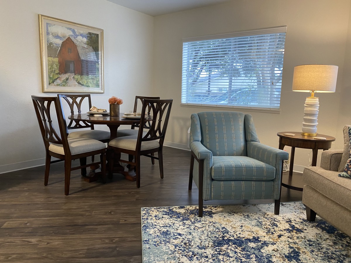 A cozy living and dining area with a blue armchair, wooden dining set, and a patterned rug.