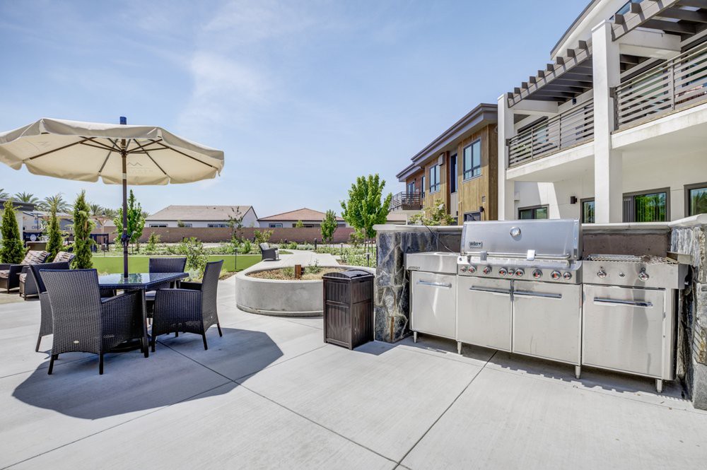 A modern outdoor patio with a grill and seating area under a sunny sky.