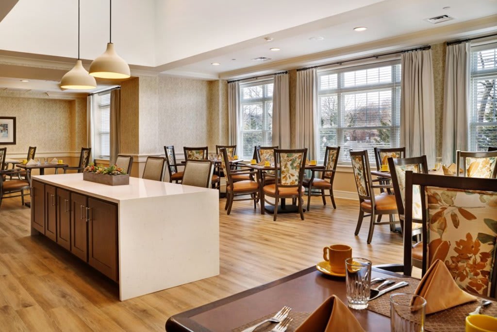 A bright, modern dining room with neatly arranged tables and chairs, illuminated by natural light from large windows.