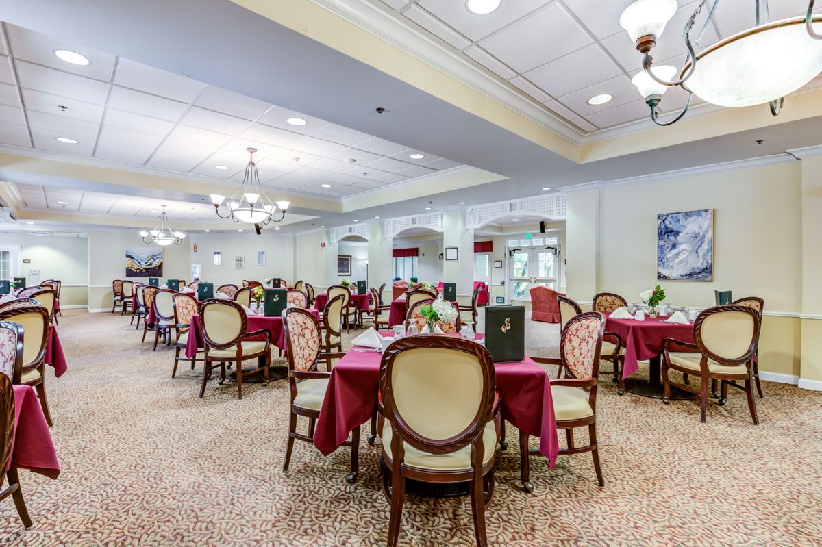 A spacious dining area featuring elegantly arranged tables with red tablecloths and classic chairs, illuminated by chandeliers.