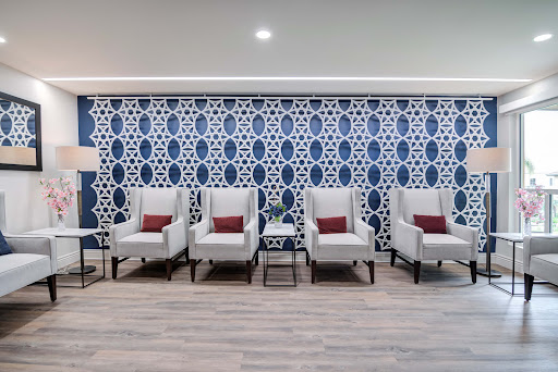 A modern waiting area featuring stylish white chairs with red cushions against a beautifully patterned blue and white wall.