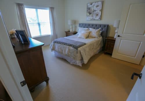A cozy bedroom with a neatly made bed, nightstands on each side, a dresser, and a large window.