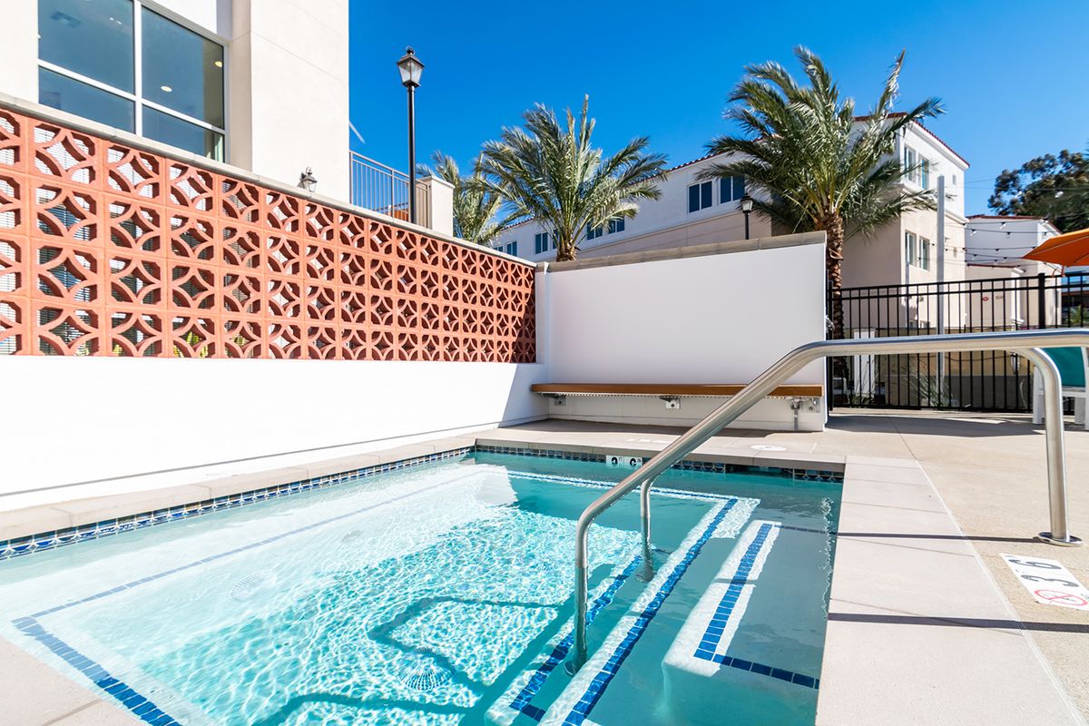 A modern outdoor swimming pool with palm trees under a clear, sunny sky.