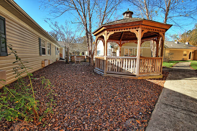 A wooden gazebo in a yard covered with autumn leaves.