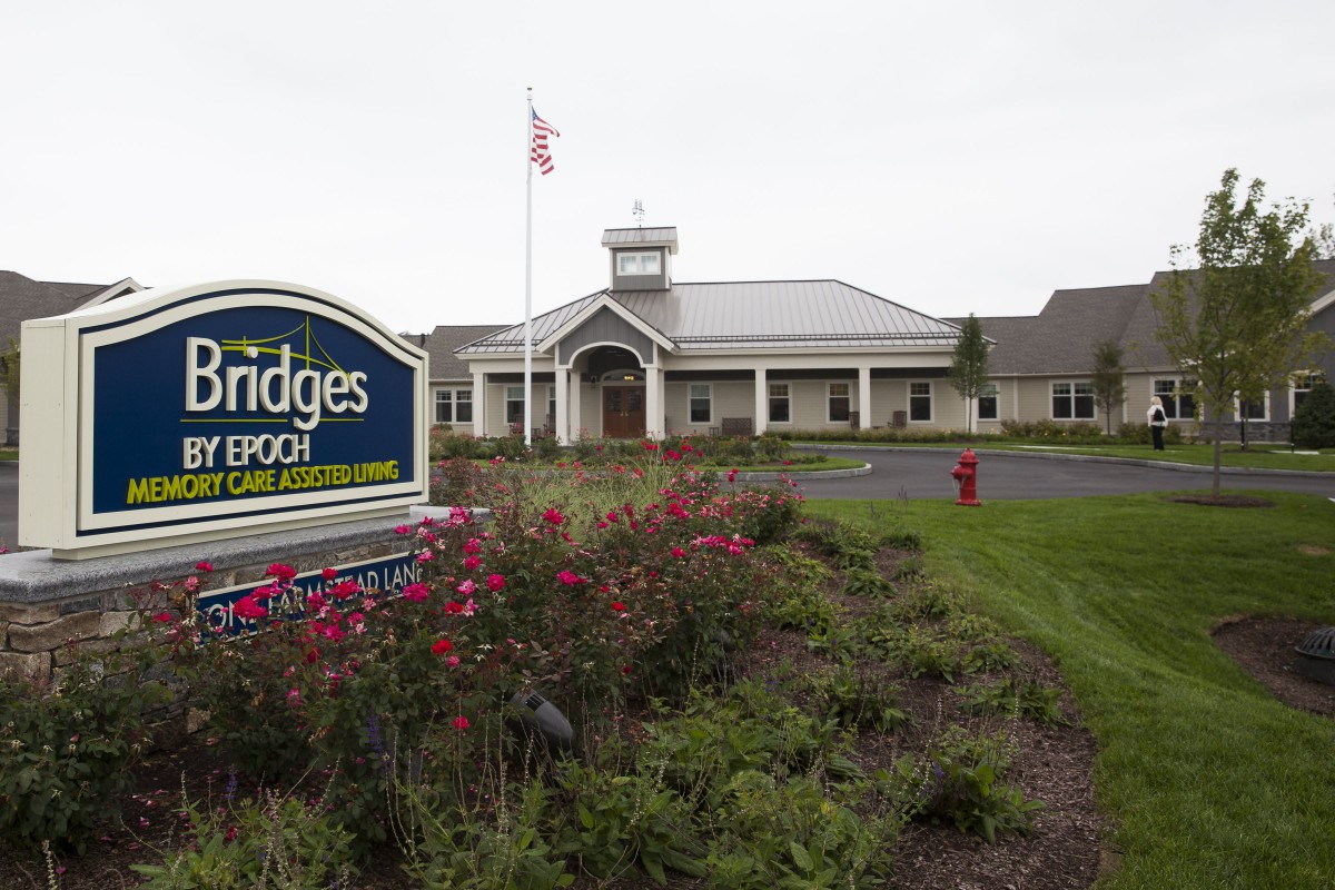 A landscaped entrance with a sign and a building in the background.