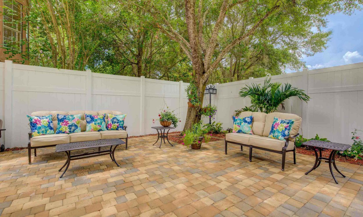 A cozy outdoor patio with cushioned seating, surrounded by a garden and fenced for privacy.