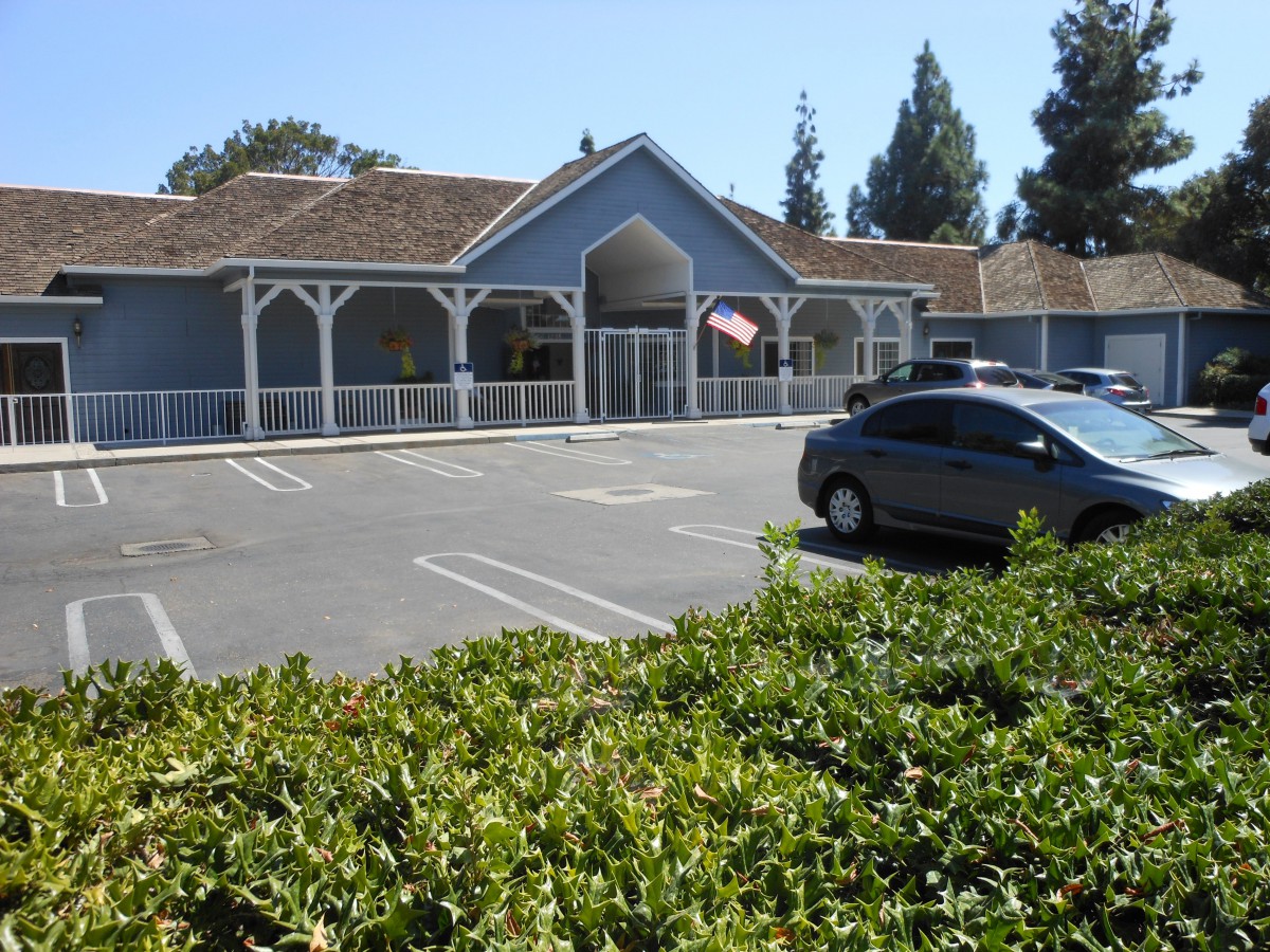 A building with a parking lot and a car parked, surrounded by trees and bushes on a sunny day.