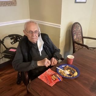 An elderly person sitting at a table with a meal in front of them.