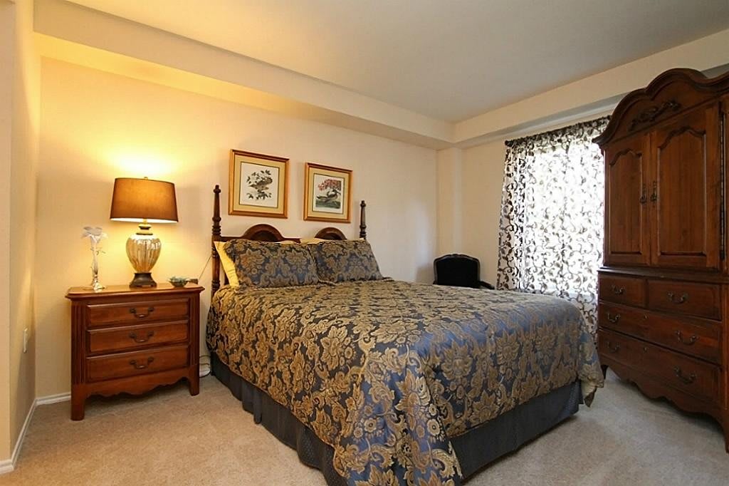 A cozy bedroom with a neatly made bed, bedside table, and a lamp by the window.