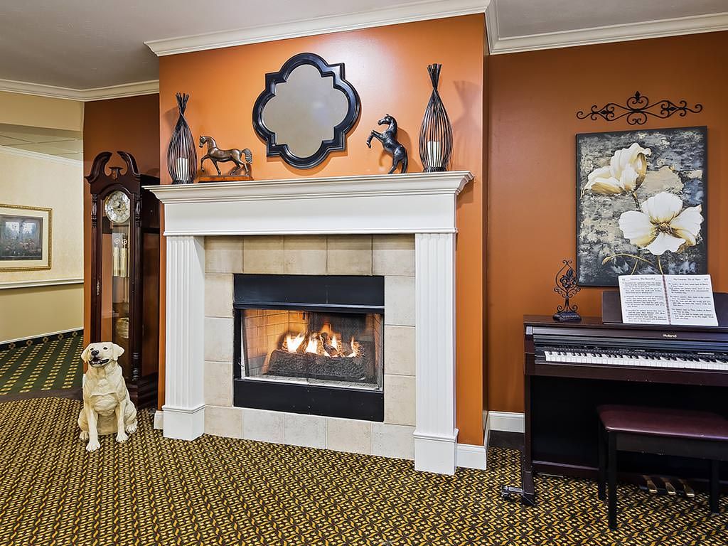 A cozy living room featuring a fireplace with decorative elements and a piano against a warm-toned wall.