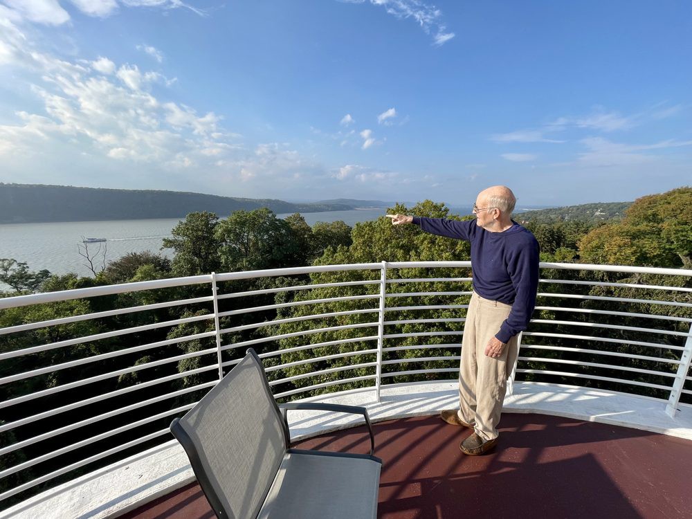 A man stands on a balcony overlooking a scenic view of a lake and trees.