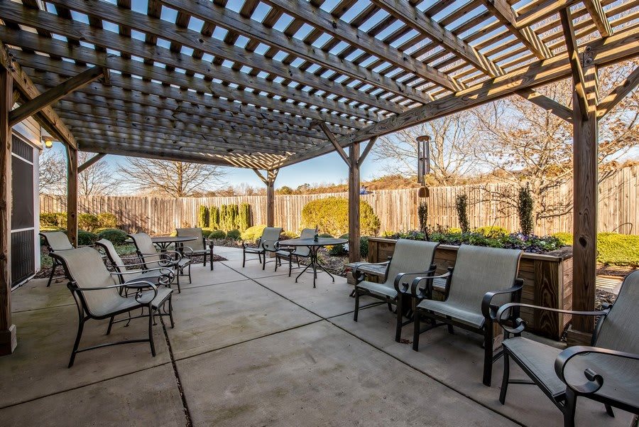 A spacious outdoor patio with a pergola, featuring comfortable seating and surrounded by well-maintained landscaping.