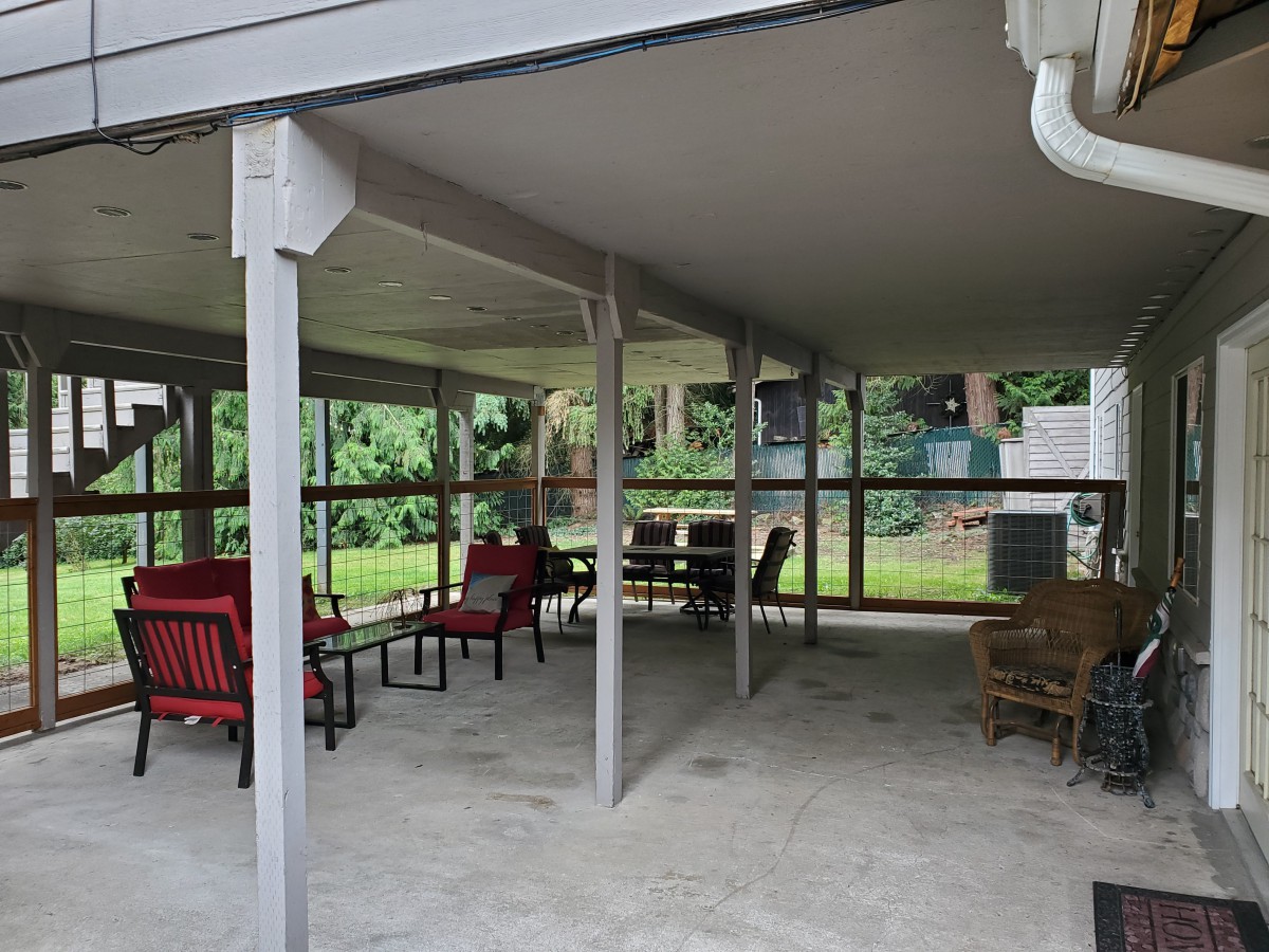 A cozy outdoor patio featuring a variety of seating options under a covered structure, surrounded by lush greenery.