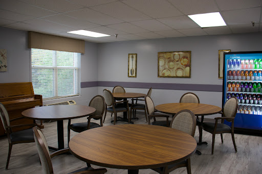 A cozy dining area featuring round wooden tables and comfortable chairs, illuminated by natural light from a nearby window.