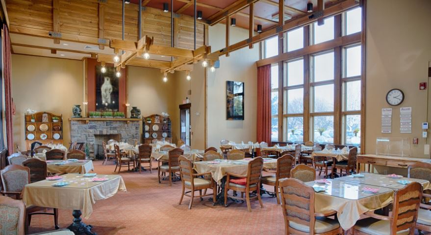 A cozy restaurant dining area featuring wooden ceilings, large windows, and neatly arranged tables and chairs.