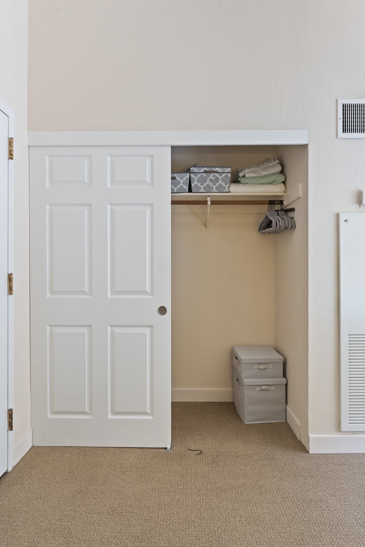 A neat and organized closet with sliding doors, featuring shelves, hangers, and storage boxes.