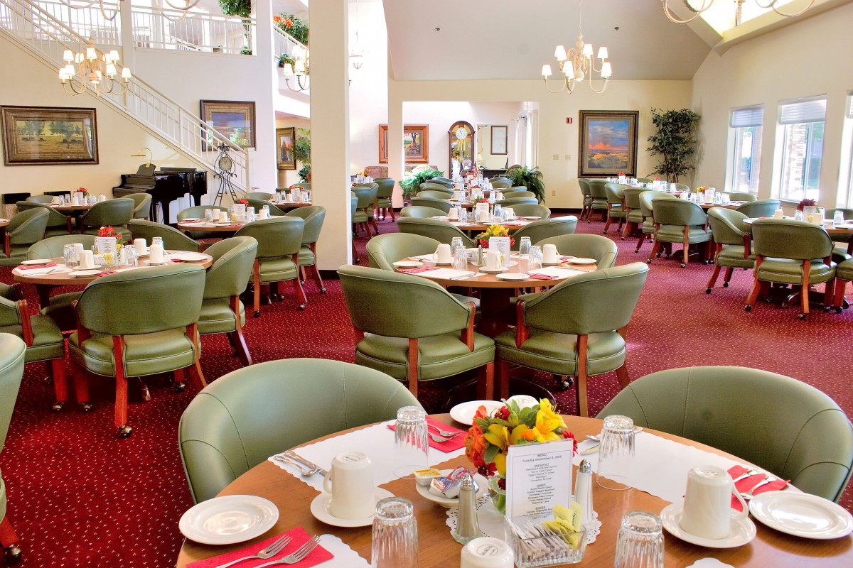 A well-lit restaurant interior with neatly arranged tables and chairs, floral centerpieces, and elegant decor.