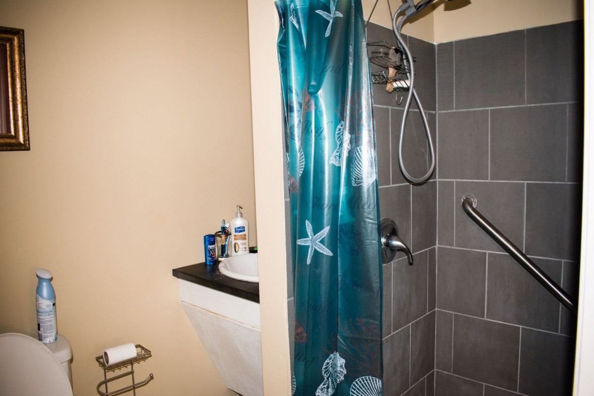 A bathroom with a tiled shower area featuring a blue shower curtain, a sink, and various toiletries.