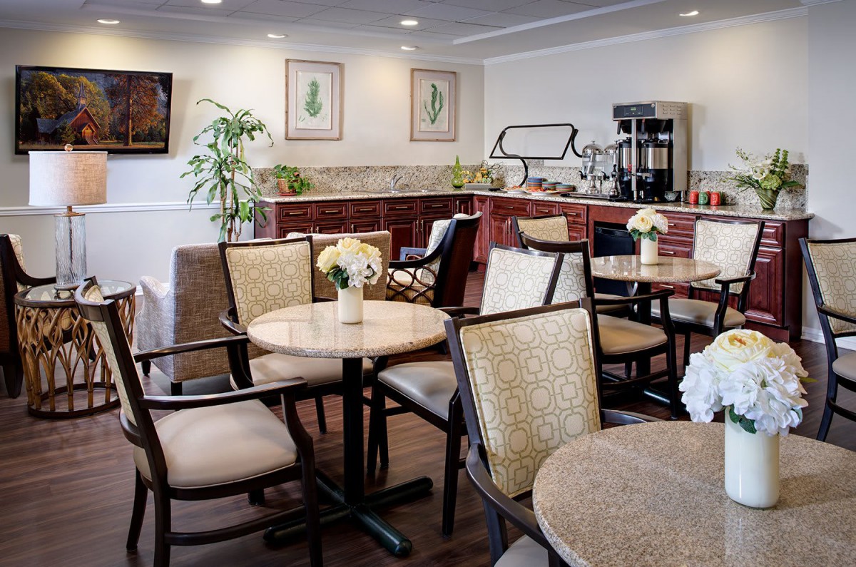 An indoor dining area with tables and chairs, featuring a coffee station and decorative plants.