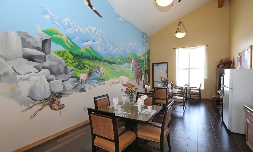 A cozy dining room featuring a vibrant nature-themed mural with mountains and forests, accompanied by elegantly set tables and chairs.
