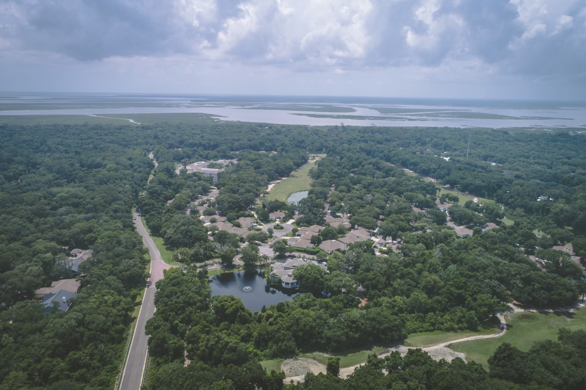 Aerial view of a lush green landscape with roads, lakes, and a cloudy sky.