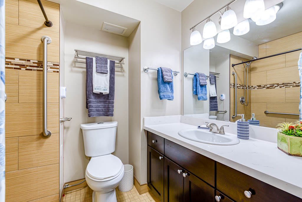 A modern bathroom featuring a toilet, sink with a large mirror, and neatly arranged towels.