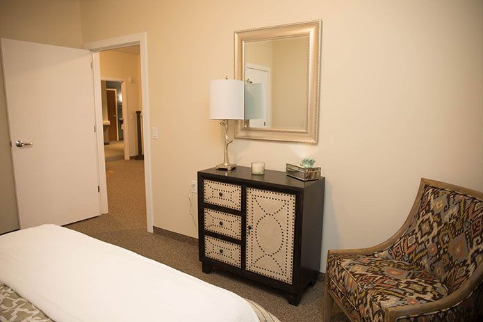 A cozy bedroom with a dresser, lamp, and mirror.