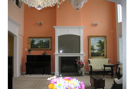 A cozy living room with a fireplace, piano, chandelier, and floral decorations.