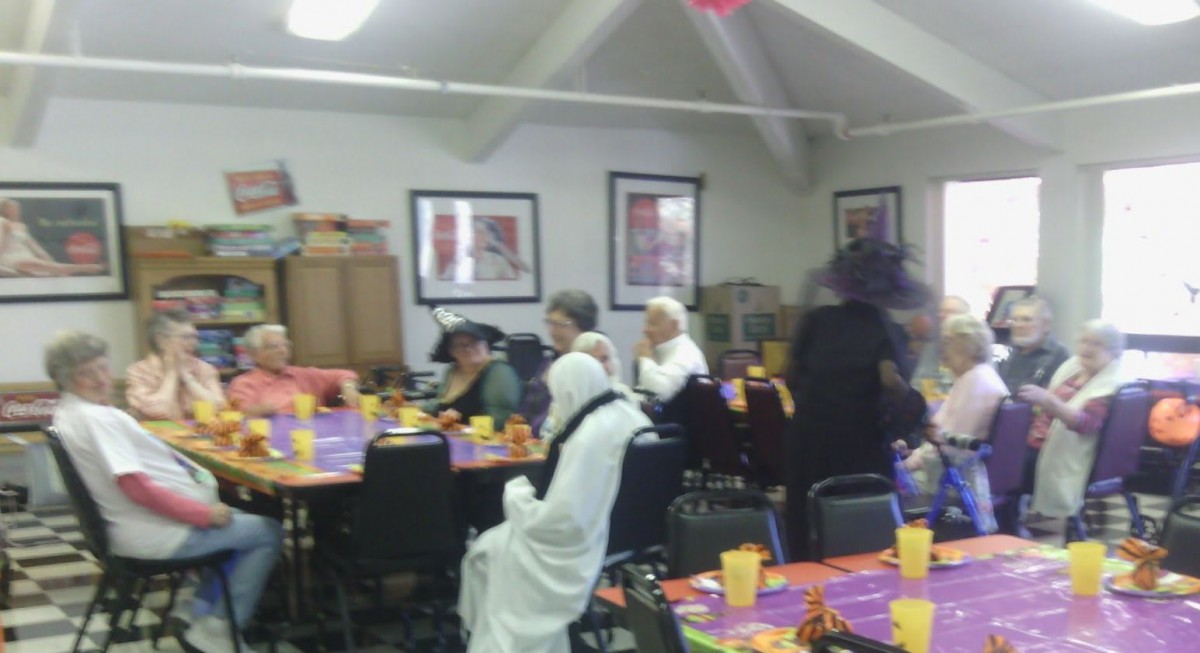 A group of people in Halloween costumes gathered at a decorated party table indoors.