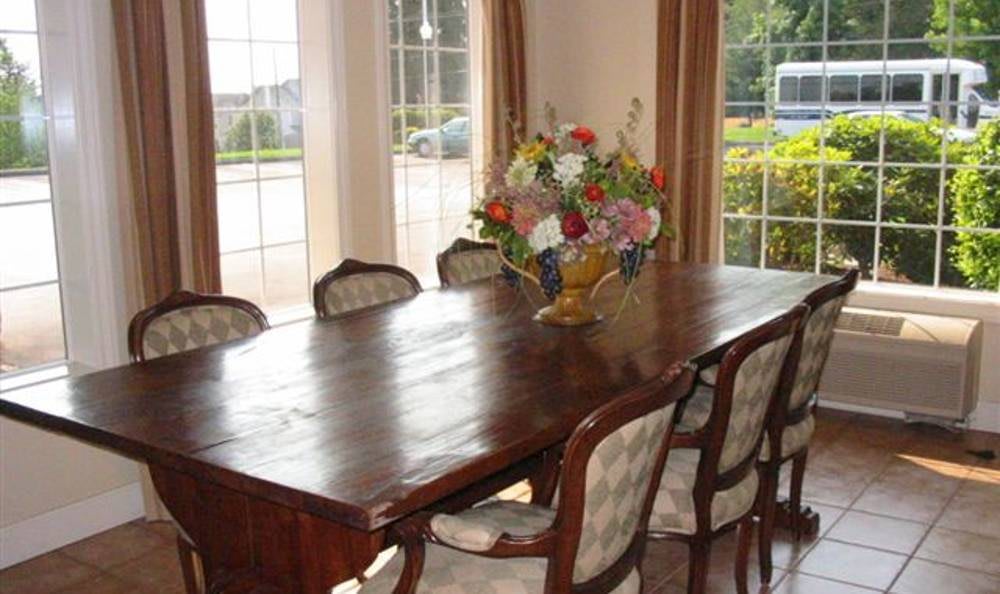 A dining room with a large wooden table and chairs, decorated with a bouquet of flowers by the window.