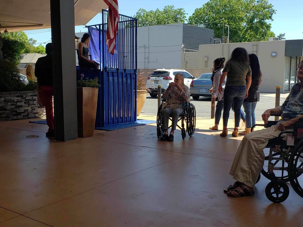 A group of people, including someone in a wheelchair, gathered near a doorway with sunlight streaming in.