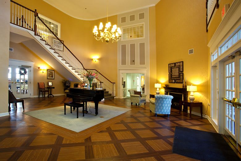 An elegant lobby featuring a grand piano, a chandelier, and a staircase.
