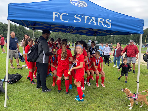 A spirited group of young athletes from FC Stars gather under their team tent, ready for action.