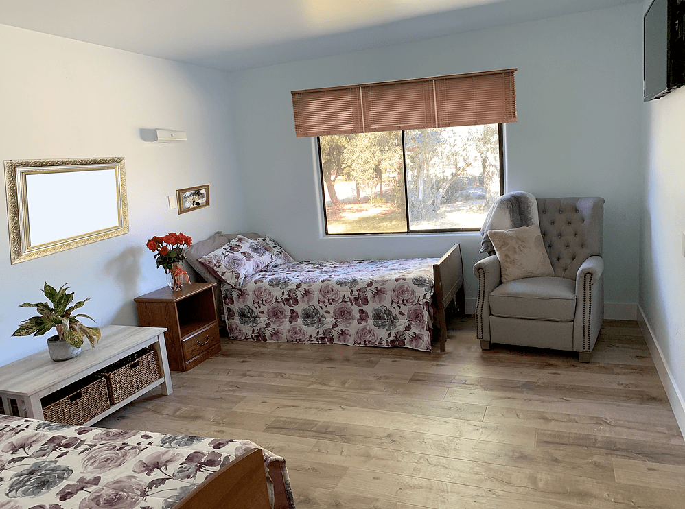 A bright and cozy bedroom with twin beds, an armchair, and a large window.