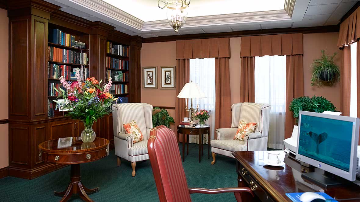A cozy office interior with classic furniture, including armchairs, a desk, and a bookshelf.