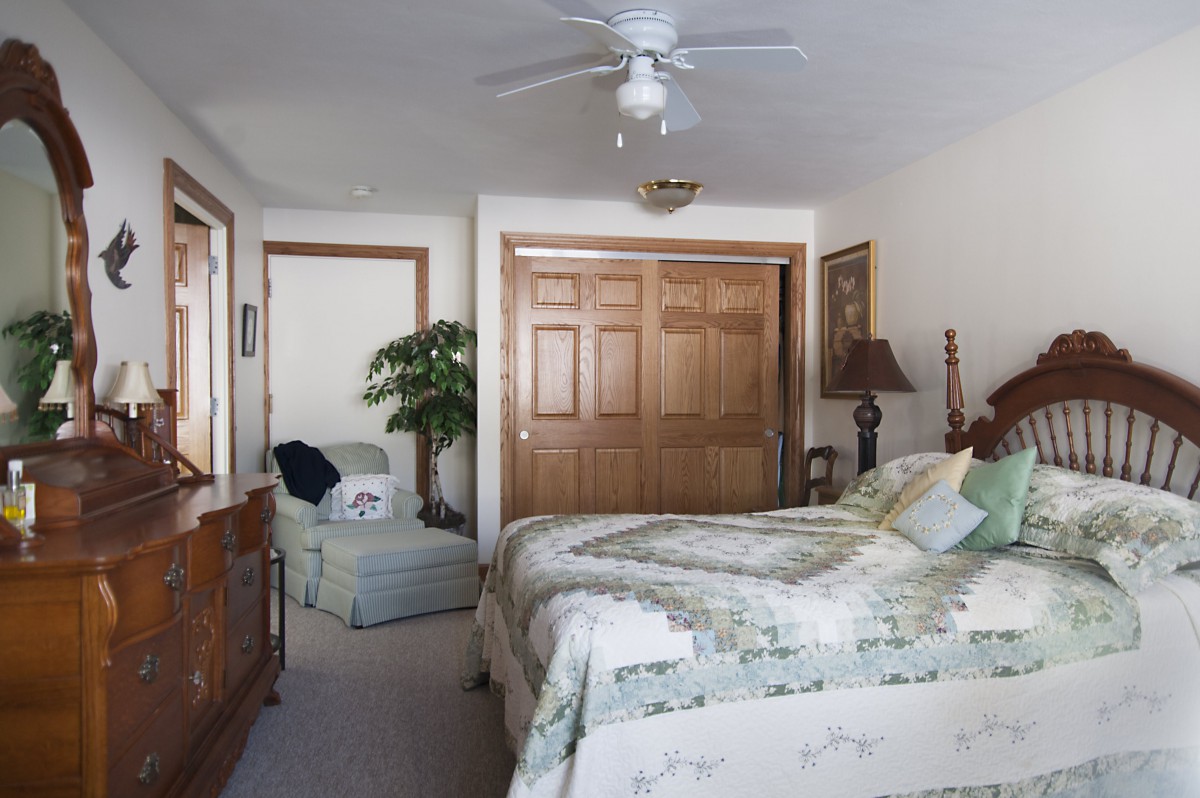 A cozy bedroom with a bed, ceiling fan, and wooden closet doors.